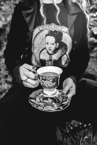 暗い服を着た女の子の手 と頭なし 公園で古い世紀のティーカップとソーサーを保持 黒と白で — ストック写真