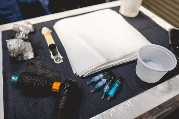 タトゥーマシン 黒インク アルコールやナプキンとプラスチックインク容器とタトゥーアーティストの作品テーブルの閉鎖 — ストック写真