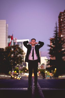 Şehir merkezinde mor bir günbatımında caddenin ortasında siyah takım elbiseli genç ve çekici bir adam.