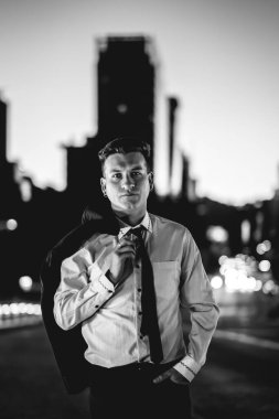 Siyah takım elbiseli ve ceketli genç ve çekici adam gün batımında şehrin göbeğinde caddenin ortasında.)