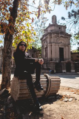 Güneşli bir günde mavi gökyüzü ve neoklasik tarzda terk edilmiş büyük antik mozolenin arasında şık, karanlık gotik bir adam.