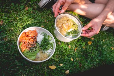 Couple lunch in the park with two 'gohan' (bowl of rice, salmon, avocado, green onion, fried chicken and sesame) and girlfriend opening one
