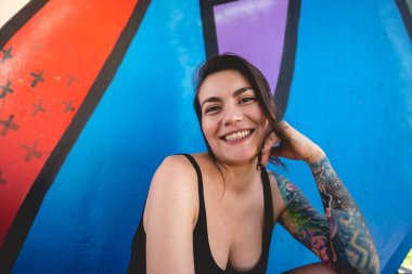 Rude, sexy, beautiful, happy and tattooed young girl smiling with black crop top in front of a colorful graffiti