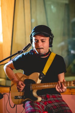 Young rocker musician with biker hat playing a cream electric guitar in a music studio