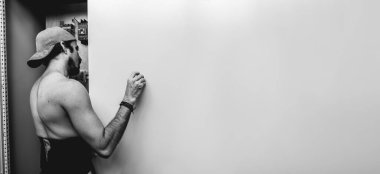 Fit young latino worker putting a screw into a hole with his hand in a steel door of a electronic area (panoramic with big copy space in black and white)