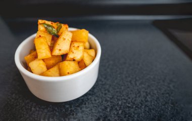 Spicy traditional turnip kimchi in white bowl in table in kitchen with big copy space (kimchi: pickled and fermented vegetables, garlic, salt, ginger, chili peppers, etc)