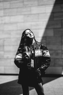 Şehirli şık: seksi esmer model sabah güneşli (siyah beyaz) büyük taş binada deri ceket ve kısa etek giyer.)