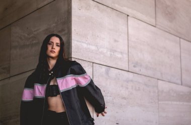 Şehir modası: genç esmer model deri ceket giyer ve sabah güneşli büyük taş bir binada uzun botlar giyer.