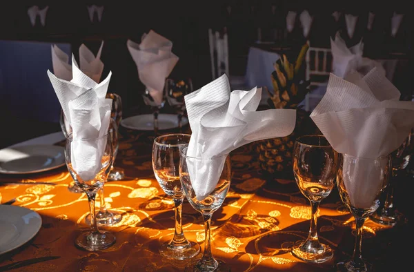 A modern wedding table set up with orange tablecloth, a pineapple, stylish glasses, and napkin decorations in the sunlight