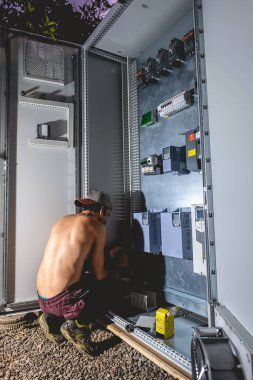 Elektronik yükleme yapan Latin işçisi gece matkapla çelik tahtaya vida yerleştiriyor.