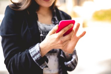Modern ve genç yönetici: güzel ve sofistike kadın şehir parkında pembe telefonunu kontrol ediyor.
