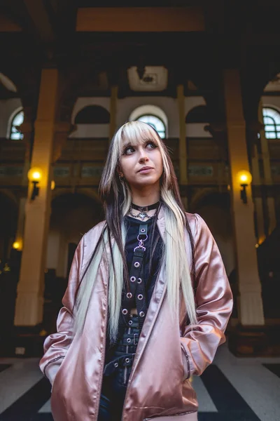 Young woman with black and blonde hair and pink jacket in the entrance of a old centuries public museum and interior with neoclassical architecture