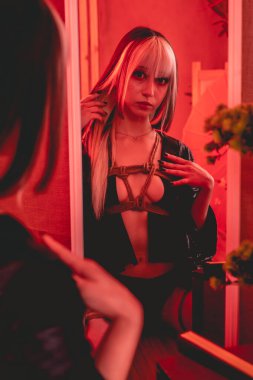 Aynadaki Shibari esaretinin güzelliği: Genç, ince ve seksi bir kadın. Vücudunda sadece küçük siyah bir kimono ve şibari bağları ve düğümleri var. Güzel kırmızı ışıklı geleneksel Japon odasında.