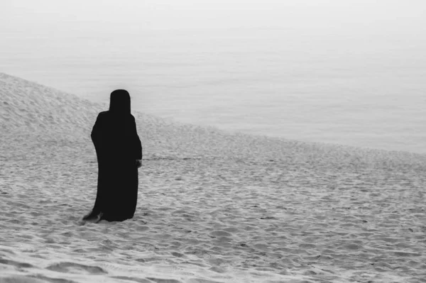 布卡之谜 在苍白的天空 黑白相间 下广阔的沙漠中 只有一个身披黑色布卡的穆斯林妇女 — 图库照片
