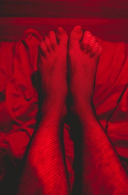 Yatakta, baştan çıkarıcı ve samimi kırmızı ışığın altında çorapların içinde seksi bacakların ve ayakların ayrıntıları.