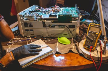 Elektronik uzmanlık alanı: siyah eldivenli ellerin elektronik ekipmanları tamir etmesi ve bir masaya not alması.