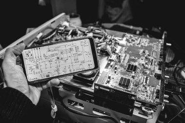 Elektronik diyagramı olan bir telefonu tutan: bir bilgisayar kartının donanımı, devreleri ve bileşenlerini inceleyen (siyah ve beyaz))