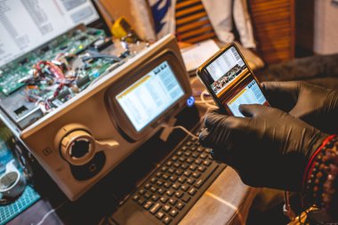 Siyah eldivenli bir el, donanım, devreler ve bilgisayar panosunun bileşenlerinin telefonuyla fotoğraf çekiyor.