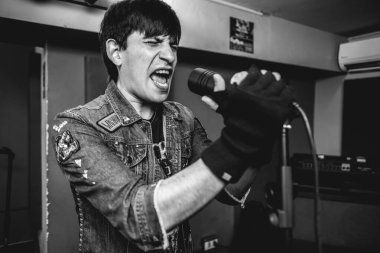 Tutkulu ve tutkulu genç rockçı vokalist bir prova odasında (siyah ve beyaz) yoğun metal performansı sırasında ham enerjisini serbest bırakıyor.)