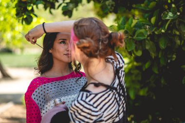 Hazırlığın güzelliği: bir makyöz güzel ve genç bir esmer mankeni parkta fotoğraf çekimine hazırlıyor.