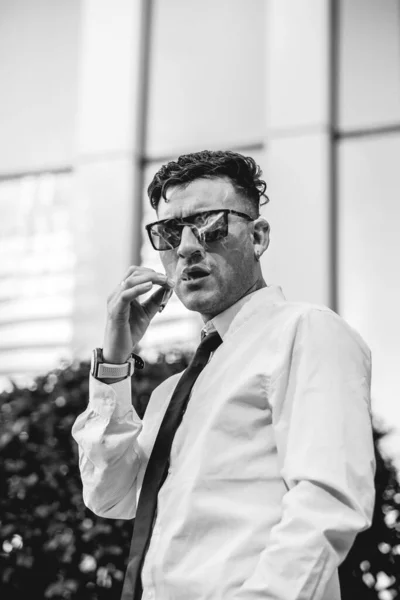Urban business lifestyle: modern and young professional with shirt and tie smoking a marijuana and tobacco joint in business district (in black and white)