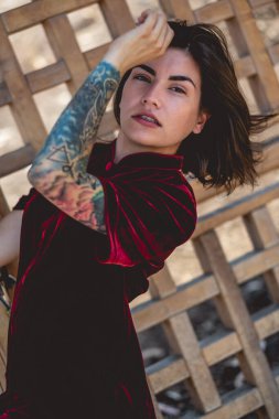 Egzotik baştan çıkarma: dövmeli seksi Latin kadın halka açık bir parkta ahşap bir kapının önünde kırmızı ipek Çin elbisesi giyiyor.