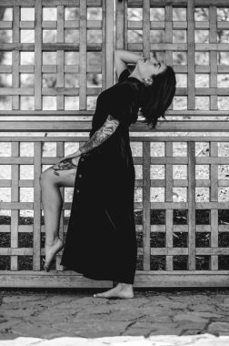 Egzotik baştan çıkarma: dövmeli genç Latin esmer kadın kırmızı ipek Çin elbisesi içinde halka açık bir parkta ahşap bir kapının önünde (siyah beyaz))