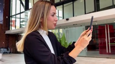 Modern bir halk şehrinde sıradan bir kahve molası: güzel ve rahat sarışın Latin yönetici kahve yudumluyor ve halka açık bir meydanda telefonla video görüşmesi yapıyor.