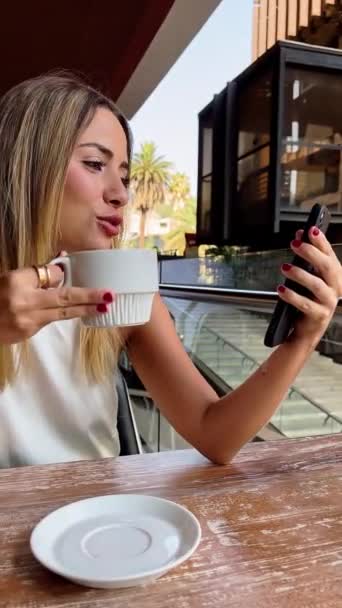 屋外の都市コーヒーでカジュアルなビジネスビデオミーティング 美しいブロンドラティーナエグゼクティブコーヒーを飲み 彼の携帯電話でビデオミーティングを持つ — ストック動画