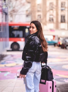 Şık seyahat ve şehir keşfi: canlı Latin esmer moda görünümlü ve pembe valizli şehir tarihi bölgesini ve şehir merkezini keşfeden