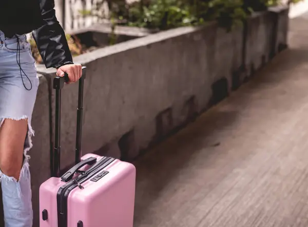 Stylish travel and urban exploration: Detail of hand of a fashion look girl and pink suitcase exploring city (with big copy space)