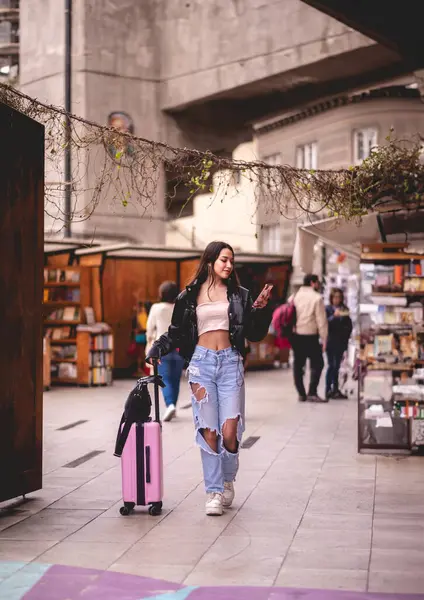 Stylish travel and urban exploration: vibrant young latina brunette with fashion look and pink suitcase exploring city historic district and downtown