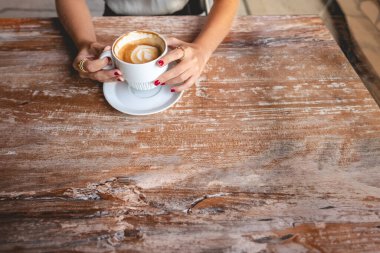 Sıradan kahve molası ayrıntıları: ahşap bir masada beyaz bir fincan kahve tutan kırmızı tırnaklı güzel kadın ellerine yakın çekim