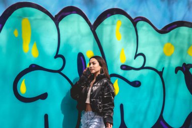 Renkli sohbet: Güzel esmer Latin kız canlı bir sokak sanat resminin önünde telefonla konuşuyor.