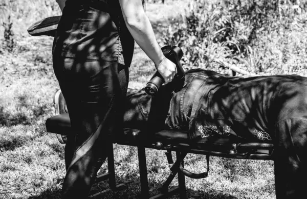 Healing touch: massage therapist\'s performing a full body massage ith a massage gun in natural surroundings (in black and white)