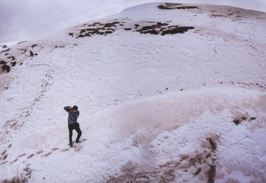 Tepeleri yakala: Genç fotoğrafçı mükemmel panoramik çekim için karlı dağ manzarasında yürüyüş yapıyor.