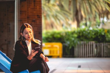 Güzel ve rahat sarışın Latin yönetici akıllı telefonu kullanıyor ve modern bir halk şehrinde gülümsüyor.