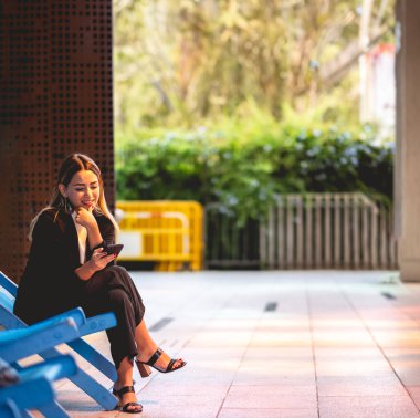 Güzel ve rahat sarışın Latin yönetici akıllı telefonu kullanıyor ve modern bir halk şehrinde gülümsüyor.