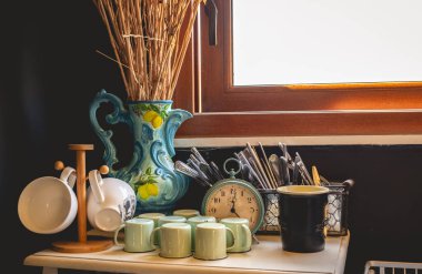 Mutfakta sabah parıltısı: pencereden içeri doğal ışık akışı, bardaklar, çatal bıçak takımı ve antika mutfak süslemeleri.