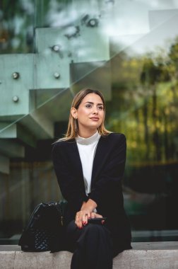 Başarılı ve güzel: rahat sarışın Latin yönetici modern bir halk meydanında oturuyor ve gülümsüyor.