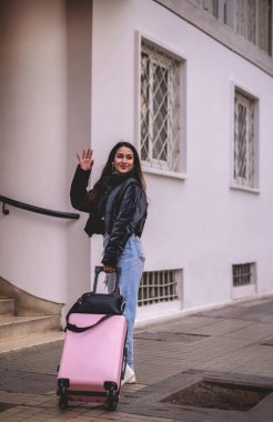 Şık seyahat: canlı Latin esmer moda görünümlü ve şehir merkezinde gezen pembe valizli.