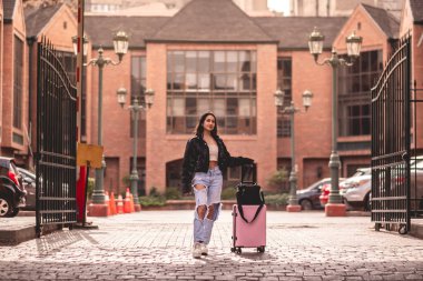 Şık seyahat: canlı Latin esmer moda görünümlü ve şehir merkezinde gezen pembe valizli.