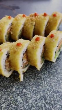 Şatafatlı suşi somon, avokado ve trüf yağıyla dolu bir tabakta, şişeden sake servisi yapan adamın arkasında.