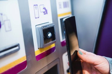 Close up of unrecognisable hand paying contact less by using smartphone. Contactless payment in a train tickets machine i