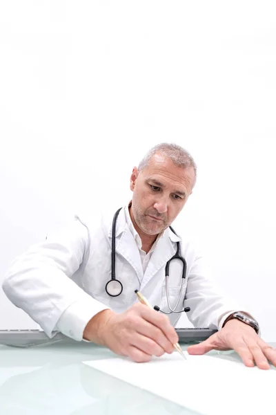 An experienced doctor writes a prescription at his office desk in a modern, clean hospital consultation room. The perfect stock image for healthcare, medical, and wellness themes, showcasing professionalism and expertise