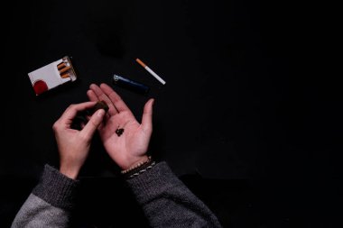 Aerial view of unrecognizable male hand rolling a hash marihuana joint in a black background studio session. A tobacco cigarette is also visible in the scene. Concept: drug consumption