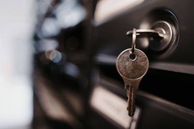Siyah posta kutularına asılmış, bulanık bir arka planı olan bir anahtarın yakın plan resmi. Gayrimenkul yatırımı, kiralık mülk, ev satın alma, paket alma, teslimat için mükemmel.