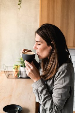 Avustralya 'da bir kafede bembeyaz içen mutlu bir kadının dikey resmi. Kahvenin üstünde Latte resmi. O yalnız ve içmeye hazır. Günlük giysiler ve fotokopi alanı. Dudaklarını köpük kaplıyor.