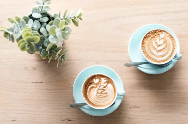 Two cups of foamy flat white coffees with latte art. Aerial shot on a wooden table. Trendy and hipster cafe. Flower draw on the foam made by the barista. No people