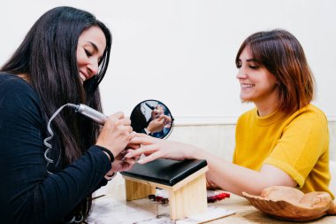 Güzellik uzmanının kadın bir müşterinin tırnak etlerini güzellik merkezinde özel bir aletle düzeltirken çekilmiş bir fotoğrafı. 30 'lu yaşlarda iki beyaz kadın. Mutlu ol ve gülümse. Beyaz arkaplan